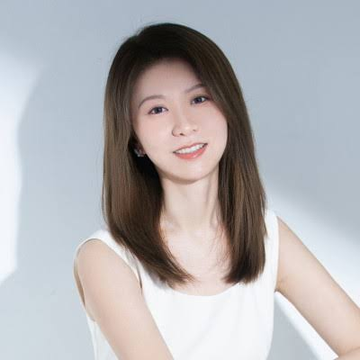 A smiling young woman with long brown hair poses for a portrait against a light gray background, wearing a white sleeveless top.