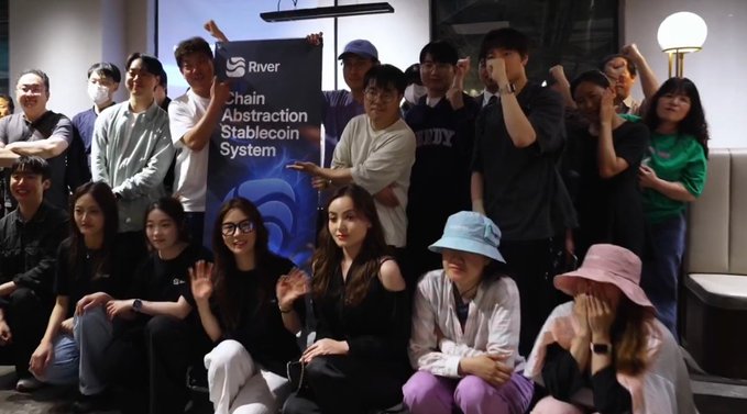 The image shows a group of people gathered together for an event or meeting. They are sitting around each other, with some individuals holding up signs that say "River" and "chain abstract scan system". The atmosphere appears to be positive and engaging as they participate in this gathering.