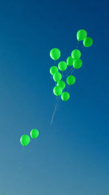 Green balloons floating against a clear blue sky, with two balloons trailing far below the main cluster.