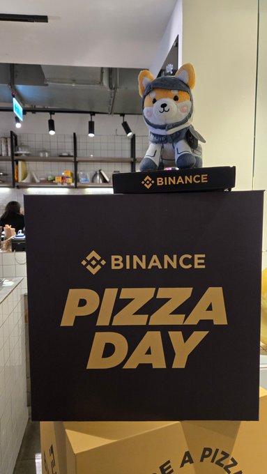 urn of tea on a table, with a "binance" sign and a stuffed animal dog nearby.