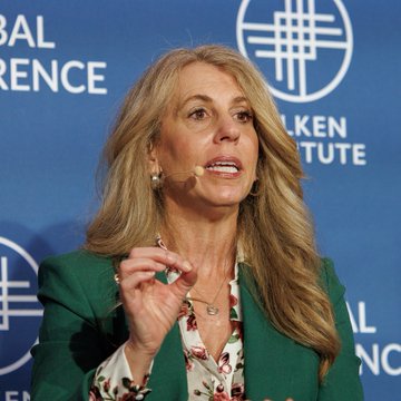 Stellar Foundation CEO Denelle Dixon speaks at the Milken Institute Global Conference (visible in the background text), appearing to gesture while discussing the difficult crypto market conditions. The image captures her mid-statement as she comments on the challenges of the current bear market.