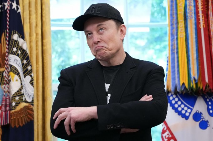 A man wearing a black "GE" cap stands with arms crossed and pursed lips inside what appears to be the Oval Office, with presidential flags visible in the background. His skeptical, disbelieving expression perfectly captures the post's reaction to people dismissing $DOGE cryptocurrency as "just an internet meme."