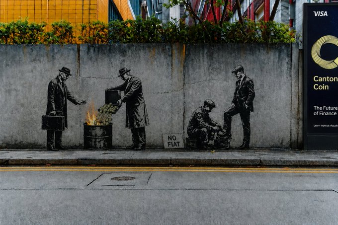 A street mural depicting businessmen in suits, including one burning money in a barrel and others sitting, with a "NO FIAT" sign, next to a Canton Coin Visa advertisement reading "The Future of Finance."