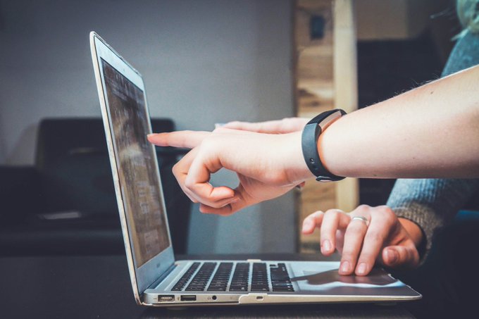 Two hands collaborate at a laptop, one pointing at the screen while the other types, with a fitness tracker visible on the wrist. The image of active digital research and data analysis visually reinforces the post's emphasis on original, research-driven content over hype.