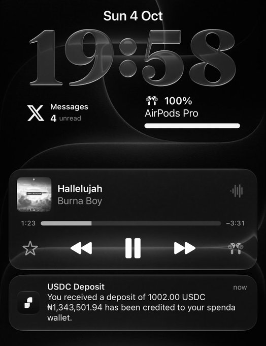 An iPhone lock screen displays the time 19:58 on Sunday, Oct 4, alongside a music widget playing "Hallelujah" by Burna Boy via AirPods Pro (100%) and a notification showing a USDC deposit of 1002.00 credited to a Spenda wallet, totaling ₦1,343,501.94—visually reinforcing the post's celebration of crossing four figures on the 4th day of Uptober.