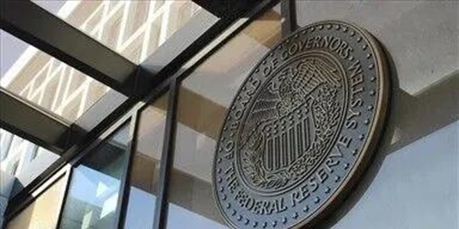 The bronze seal of 'THE FEDERAL RESERVE SYSTEM' and 'THE BOARD OF GOVERNORS' mounted on the exterior of a glass building.