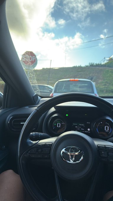 The image shows the interior of a Toyota vehicle with the digital dashboard displaying "0" mph and the steering wheel visible, while outside the windshield a stop sign is seen under sunny skies. The post's mention of dropping a $SOL address suggests the driver is ready to send their Solana cryptocurrency wallet address, with the stationary car at a stop sign symbolizing a moment to pause and share the address.