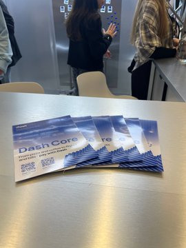 Four "DashCore" brochures fan out on a metal table at the G GATE Conf, with attendees mingling in the background following two days of partnership-focused meetings with payment providers, iGaming, and crypto teams.
