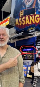 A bearded man in a green shirt points toward a storefront sign reading 'ASSANGE' while standing outside what appears to be a memorabilia shop with signs for 'Satoshi' and 'Logos' visible.