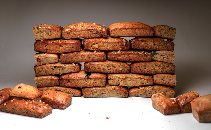A stack of rectangular fruit and nut cake bars piled against a gray background, with smaller pieces scattered in the foreground.