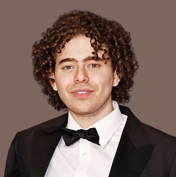 A young man with curly brown hair and a mustache is dressed in formal attire featuring a black tuxedo, white shirt, and black bow tie, posing against a solid mauve background. The image appears unrelated to the post about JPMorgan and Polymarket, as no visible text, logos, or identifying markers connect the portrait to the banking or cryptocurrency news story.