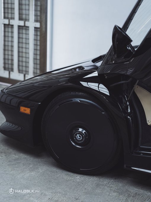 Close-up shot of a black sports car's front wheel and side profile, watermarked 'HALOBLK.PH'.