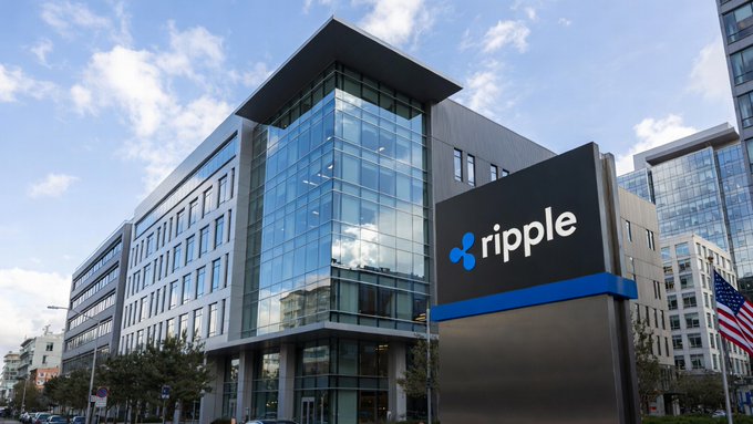 A modern multi-story office building with glass facades featuring a large 'ripple' sign and logo at the entrance, with an American flag visible nearby.