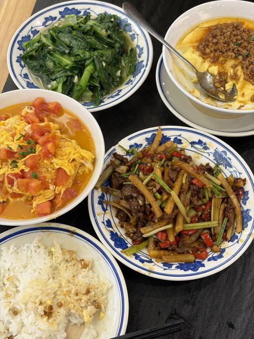 A spread of Chinese home-cooked dishes includes stir-fried greens, tomato and egg soup, steamed egg with minced meat, stir-fried beef with celery and chilies, and a bowl of white rice.