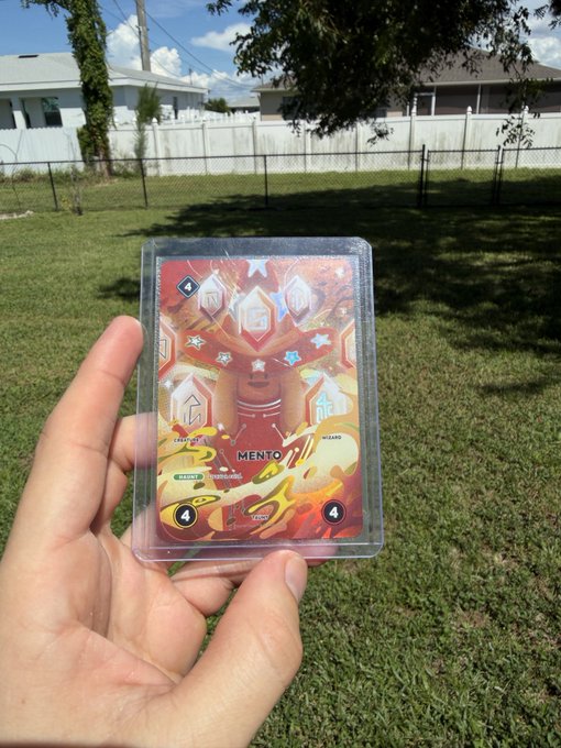 A hand holds up a holographic 'Mentor' trading card encased in a protective sleeve, with a sunny backyard and white fence in the background.