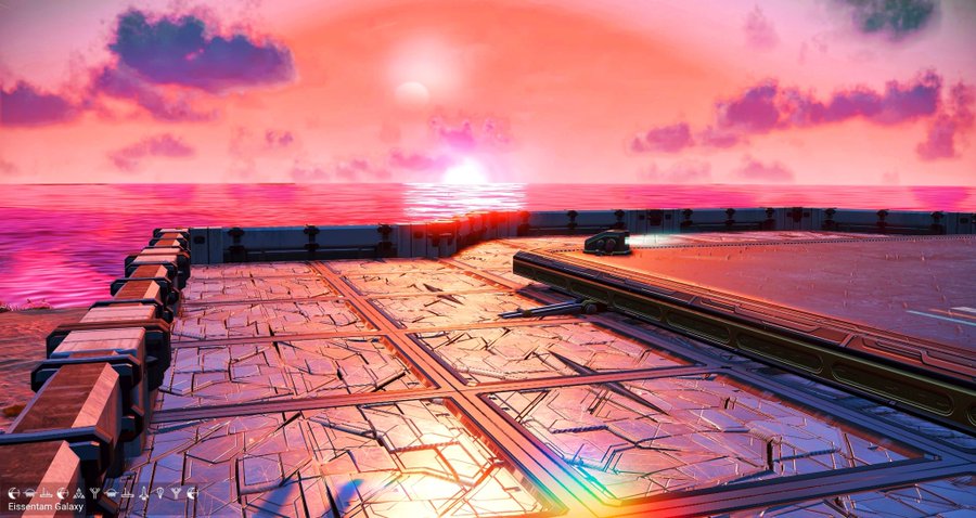 A vibrant sunset over an ocean viewed from a metallic platform or pier, with pink and orange clouds reflecting on the water's surface.