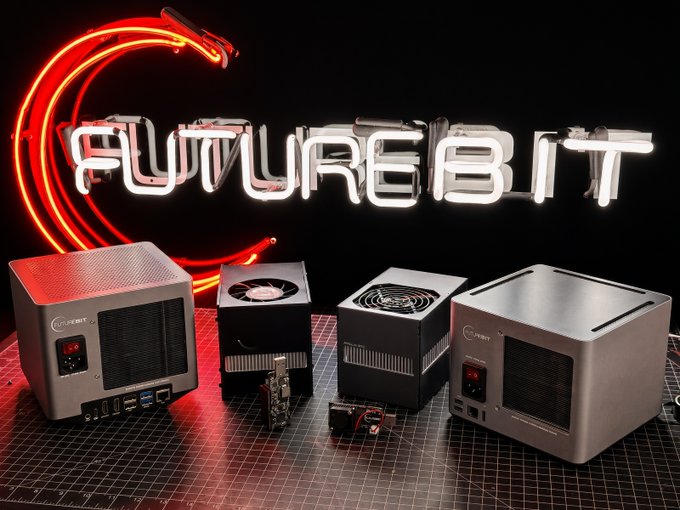 A product display featuring a neon sign reading 'FUTUREBIT' above several silver and black cryptocurrency mining devices arranged on a grid mat.