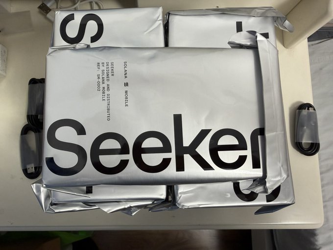 An unopened silver shipping package branded 'Seeker' with 'SOLANA MOBILE' and 'EXPLORER' text rests on a table, labeled as designed and distributed by Solana Mobile.