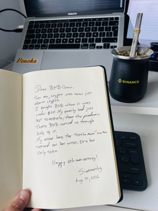 A handwritten letter addressed to "BNB Chain" on a notebook page, sharing a personal testimonial about buying BNB under $20 during the pandemic and the family tattooing "Crypto Moon" on their mom's wrist, alongside a black Binance-branded mate cup and an open MacBook. The heartfelt note celebrates BNB Chain's 6th anniversary, signed "Simão Mortágua, Aug 31, 2026."