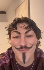 A person wearing a Guy Fawkes mask and a striped shirt takes a selfie, appearing to channel the chaotic "just one more spin" energy of gamblers clinging to lucky rituals before going broke on Sweet Bonanza.