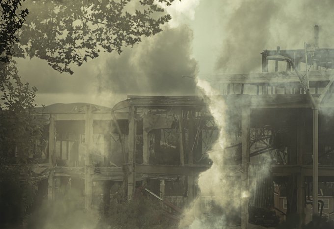 A desolate, sepia-toned photograph showing the skeletal remains of a destroyed, multi-story building enveloped in heavy smoke and debris.