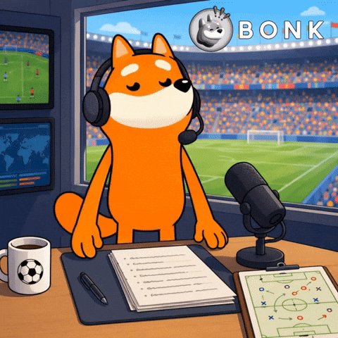 The image features a cartoon character, possibly a dog or a cat, wearing headphones while sitting at a desk with papers and other items such as a cup of coffee and a microphone. The scene appears to be set during a game, as indicated by the presence of sports balls in the background. The caption "Game time" suggests that this image is related to a sports event or a live broadcast featuring the cartoon character as a reporter or commentator.