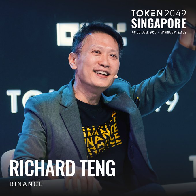 Richard Teng, identified as Co-CEO of Binance, smiles with his arm raised at the TOKEN2049 Singapore conference banner, scheduled for 7-8 October 2026 at Marina Bay Sands.