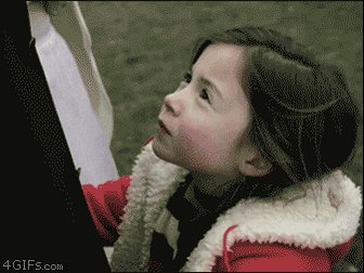 The image shows a young girl wearing a red coat and hat, standing outside and leaning against something while looking up with a serious expression on her face. The surrounding area appears to be outdoors, possibly in an outdoor setting or near a park, as suggested by the phrase "low key". This low-key setting contrasts with the main focus of the image, which is the little girl's intense gaze upwards and her serious facial expression.