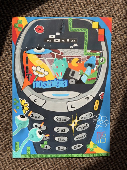 A colorful artwork on a cardboard notebook depicting a Nokia phone with the word 'nostalgia' and various retro elements like mushrooms, eyes, and a caterpillar.