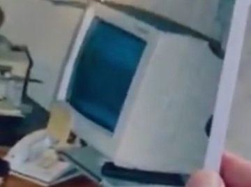 A blurry video still showing a hand holding up what appears to be an old computer monitor or CRT display in a cluttered room.