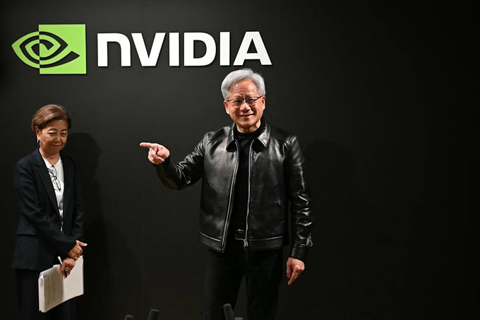 Two people pose in front of a black wall featuring the green and white NVIDIA logo.