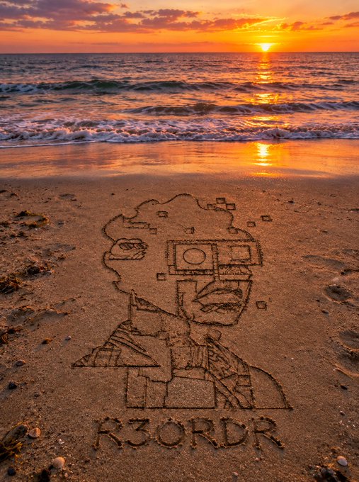 A serene beach sunset serves as the backdrop for an intricate sand drawing of a stylized figure wearing futuristic goggles, with "R3ORDR" etched below—visually echoing the post's invitation to spot signals from the @R3ORDR account while relaxing. The creative artwork ties the weekend's chill vibe to a treasure-hunt moment, where the beach itself becomes the canvas for discovery.