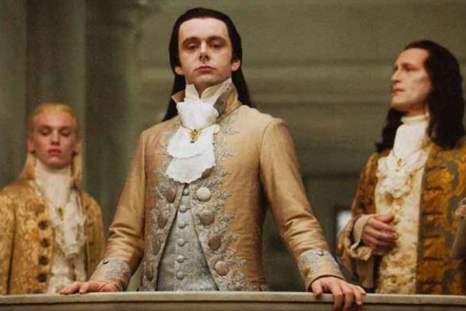 Three men in elaborate 18th-century European aristocratic attire with powdered wigs and ornate embroidered jackets, appearing to be from a period film.