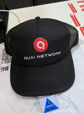 A black trucker hat with a red 'Q' logo and 'QUAI NETWORK' text displayed on a white surface.