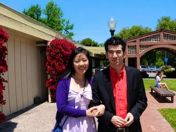 A smiling couple poses in front of a building adorned with vibrant red roses, with an older man sitting on a bench in the background. The accompanying post emphasizes that Pi Network was created in the United States, suggesting that its American origins imply legitimacy due to the country's strict financial and legal oversight.