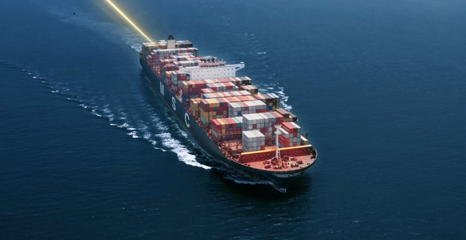 An aerial view of a large container ship loaded with colorful shipping containers sailing through deep blue ocean waters, with a beam of light extending from the ship.