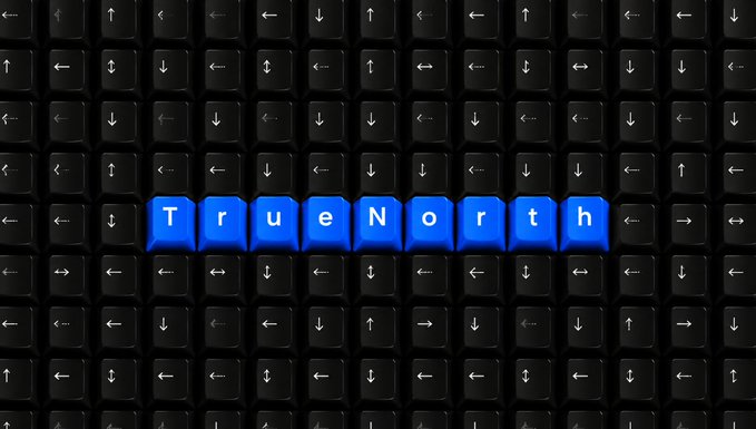 A close-up of a black computer keyboard with blue backlit keys forming the word "TrueNorth" across the directional arrow keys.
