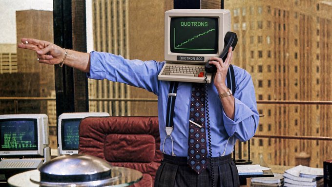 A person in a blue shirt and patterned tie wears a vintage computer monitor with "QUOTRON 800" and "QUOTRONS" displayed on the screen as a head, holding a phone receiver while pointing.