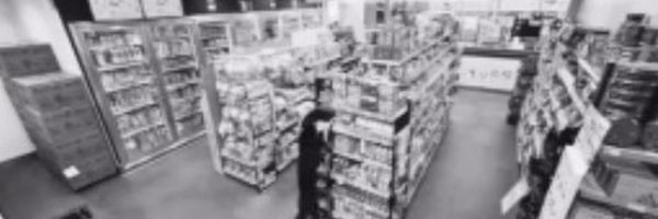 A blurry black-and-white surveillance-style image shows the interior of a store with aisles of shelving stocked with products. In the center aisle, a figure dressed in dark clothing appears to be standing in an unusual pose, which the accompanying post suggests is meant to look like an ape character as part of an internet meme shared on a Toronto TV broadcast, with the meme tied to the cryptocurrency contract address CA: 0xccfbcd3bf85d8657a6bbd10b8c81c99f13207777.