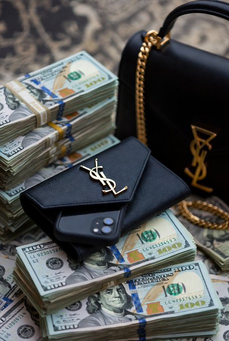 A luxury lifestyle flat-lay showing stacks of bundled $100 bills surrounding a black YSL (Saint Laurent) phone case and handbag with gold chain and logo accents.