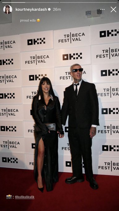 The image features a man and woman standing together, both dressed in black attire with the woman wearing high heels. They are posing for a picture against a backdrop of a white wall adorned with logos such as "okx" and " Tribeca Festival". The caption on the image reads "great marketing @okx kardashians", indicating that this photo was taken by a marketing team to promote an event or brand related to the "okx kardashians" line.