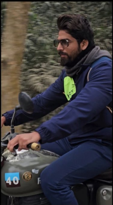 A bearded man with glasses rides a vintage motorcycle, wearing a navy blue tracksuit with a bright neon green accent patch on the chest.