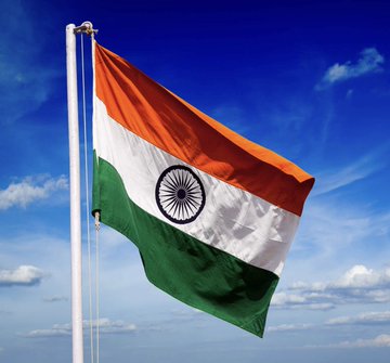 The image shows the Indian national flag (the Tiranga) waving against a blue sky, featuring its saffron, white, and green horizontal stripes with the navy blue Ashoka Chakra wheel in the center. The flag visually represents India as a nation, complementing the post's discussion about India becoming a futures-first crypto market, where crypto futures now account for nearly 80% of the country's trading volume due to factors like high taxes, weak altcoin performance, and leverage trading.
