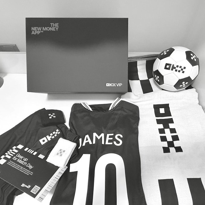 The image shows a collection of sports merchandise, including jerseys, towels, and other items related to soccer. The merchandise includes a black jersey with the number 10, a soccer ball, and a towel featuring the OKX logo. The items are arranged on a table or countertop, suggesting that they might be for sale or being displayed as part of an event or promotion.