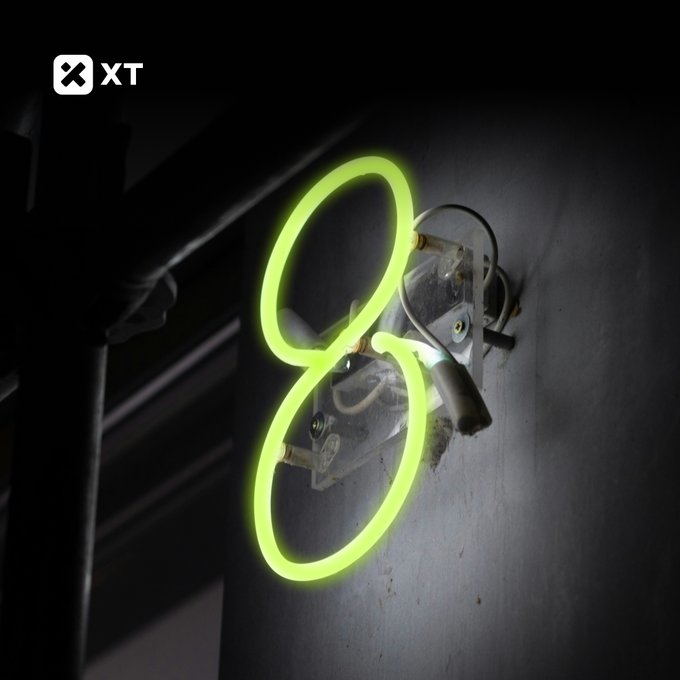 XT logo in the top-left corner over a dark image of a neon green figure-8 light installation mounted on a wall with an exposed spotlight fixture.