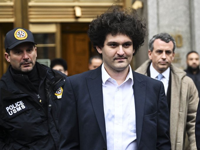 Sam Bankman-Fried exits a courthouse escorted by a U.S. Marshals Service officer. The image relates to the post by depicting the FTX founder, whose potential clemency was the subject of the Senate's unanimous resolution.