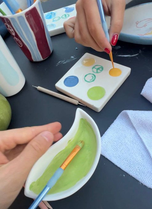 Close-up of hands painting with green paint from a ceramic palette at an art class.