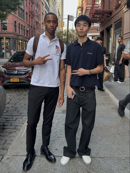 Two stylishly dressed young men pose on a NYC street during fashion week, with one wearing a white polo shirt and the other sporting a navy "Willy White" tee and black pants, capturing the trendy urban vibe mentioned in the post about meeting Ansem and Kimchi.