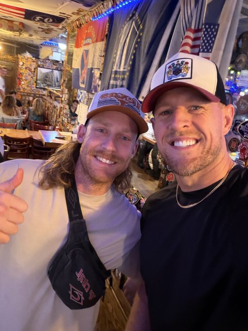 Two men smile for a selfie inside a restaurant, with one wearing a white cap featuring "USA" and the other wearing a black cap with an American flag logo and what appears to be an emblem. Given the context of the post, this likely shows the host of a Shuffle lottery stream meeting a fan in person, with their patriotic attire fitting the stream's celebratory moment.