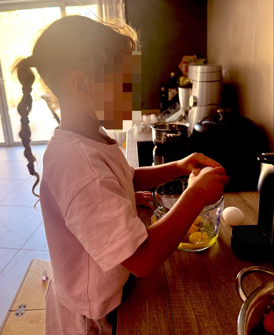 A young girl with a long braid carefully cracks an egg into a glass bowl in a sunlit kitchen, playing the role of caretaker while her mother recovers from being sick for four days.